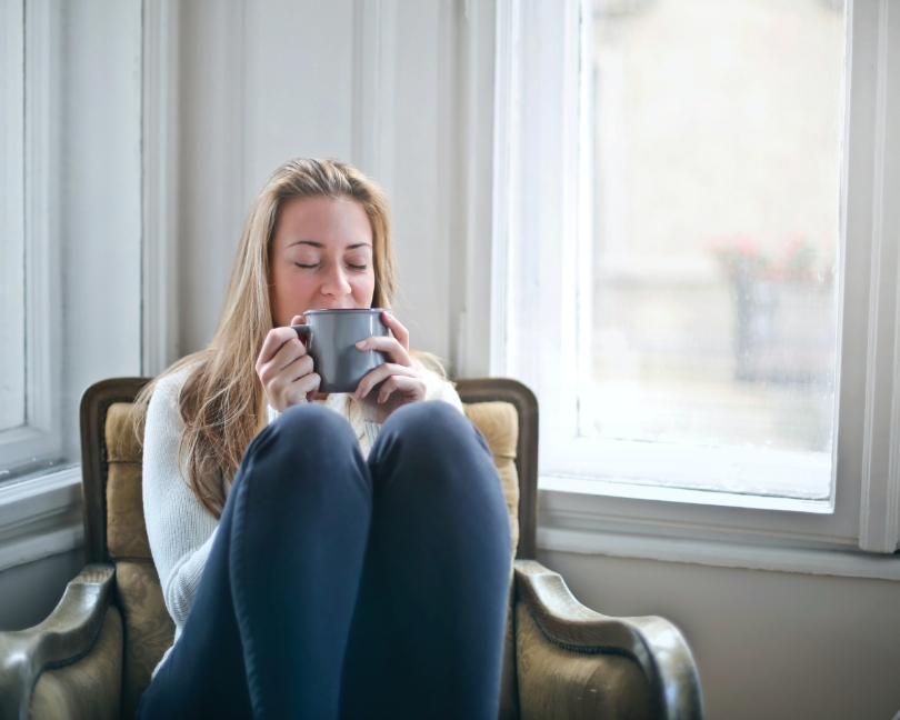 Una joven sentada en un sillón, bebiendo un té de hierbas caliente.